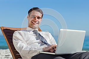 Cheerful young businessman lying on a deck chair with his computer