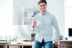 Cheerful young businessman showing thumbs up in office
