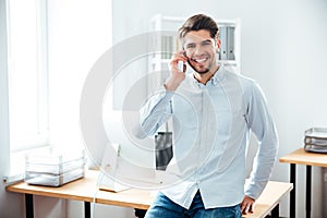 Cheerful young businessman talking on mobile phone in office