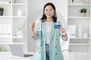 Cheerful young caucasian businesswoman in suit hold credit card and house