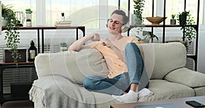 Cheerful young caucasian man listening music with headphones on sofa at home