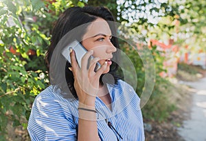 Cheerful young Caucasian woman wearing blue shirt talking on mobile phone about new project. People, lifestyle and business