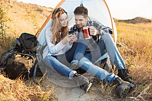 Cheerful young couple camping, sitting