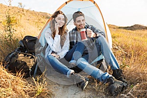 Cheerful young couple camping, sitting