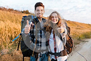 Cheerful young couple carrying backpacks hiking together