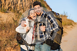 Cheerful young couple carrying backpacks hiking together