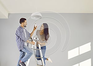 Cheerful young couple changing light bulb in apartment