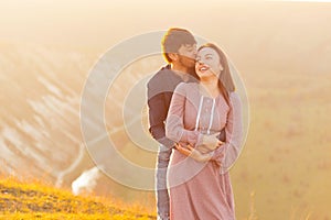 Cheerful young couple embracing outdoor in nature on the hills and having good time together at sunset