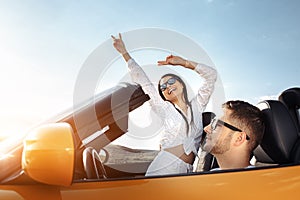 Cheerful young couple going on a long drive in a convertible car on the sunset. Freedom, travel and love concept.