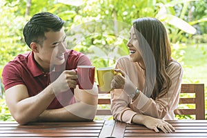 Cheerful couple holding cup of coffee or tea while sitting on chair in the garden at home. Romantic lover enjoying drink hot