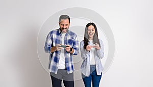 Cheerful young couple laughing and playing video games on mobile phones isolated over white background