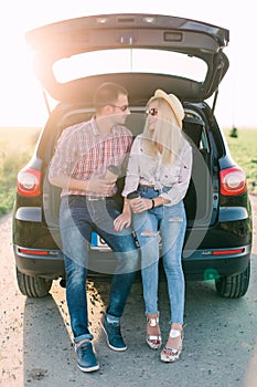 Cheerful young couple looking at mobile phone together while both sitting at the trunk of retro minivan