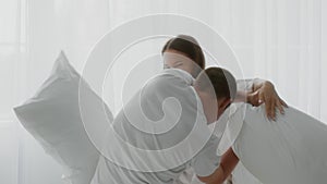 Cheerful young couple pillow fighting in bedroom, having fun at home
