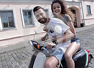 Cheerful young couple riding a scooter and having fun