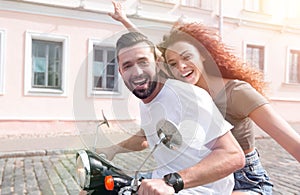 Cheerful young couple riding a scooter and having fun