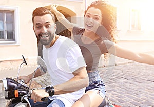 Cheerful young couple riding a scooter and having fun