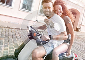 Cheerful young couple riding a scooter and having fun