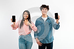 Cheerful Young Couple Showing Cellphones Empty Screens On White Background