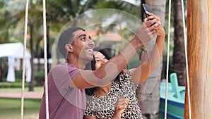 Cheerful young couple on a swing smiling, taking selfie photos with smartphone.