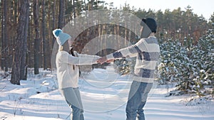 Cheerful young couple of tourists holding hands spinning in slow motion on snowy road in winter forest. Happy excited