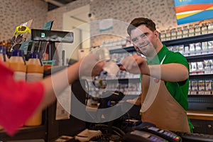 Cheerful young Down Syndrome employee taking cash payment from costumer in gas station cafe.