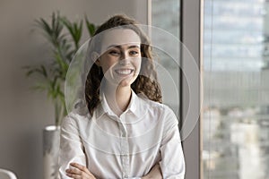 Cheerful young employee woman posing in office with hands folded