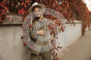 Cheerful young fair-skinned woman in fashionable hat poses modestly during trip abroad.