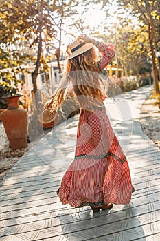 Cheerful young fashionable woman in hat having fun outdoors at sunset