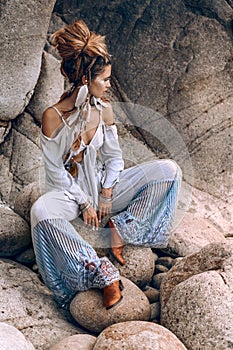 Cheerful young fashionable woman sitting on the stone beach