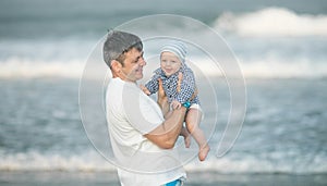 Cheerful young father with his infant son having fun together by seaside, dad throwing up kid in the air