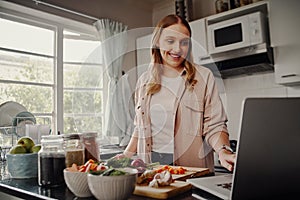 Cheerful young female blogger browsing for online recipe to prepare salad of fresh vegetables and post on social media