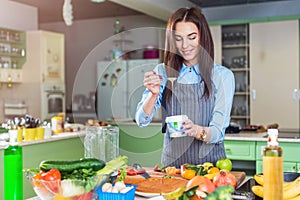 Cheerful young female chef cooking dessert adding condensed milk in dish in her kitchen