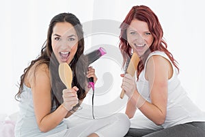 Cheerful young female friends singing into hairbrushes