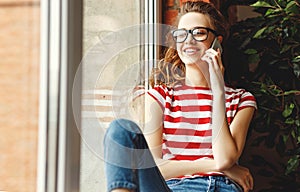 Cheerful young female student talking on phone while lounging on window sill in university