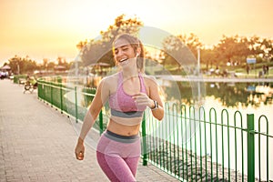 Cheerful young fit woman in sportswear wearing wireless earbuds running outdoor