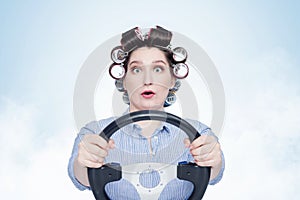 Cheerful young girl in curlers with steering wheel. Front view. Housewife driving a car.