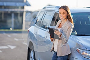 Cheerful young girl is holding laptop near vehicle