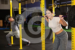 Cheerful young girl performing exercises with barbell at gym