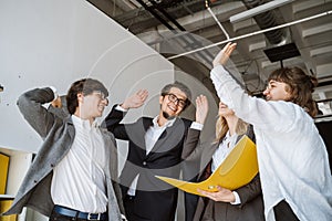 Cheerful young group of people standing in the office and giving high five