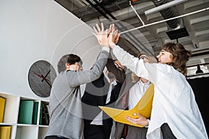 Cheerful young group of people standing in the office and giving high five