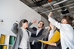 Cheerful young group of people standing in the office and giving high five