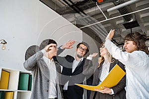 Cheerful young group of people standing in the office and giving high five