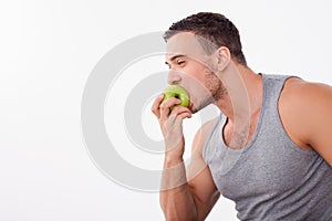 Cheerful young guy is biting a fruit greedily