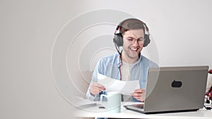 Cheerful young guy in headphones having video conferevce at home