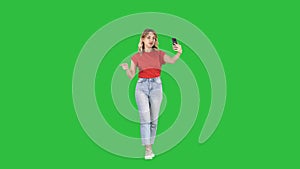 Cheerful young hipster girl streaming video for internet blog while walking on a green screen, chroma key.