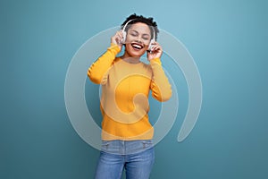 cheerful young hispanic business woman with black curly hair listening to music in white headphones