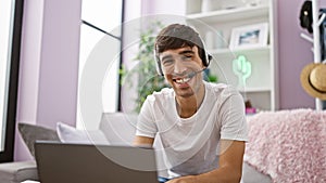 Cheerful young hispanic man seamlessly telecommuting from his relaxing living room sofa - joyfully using headphones and laptop as