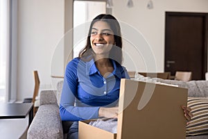 Cheerful young Indian customer girl unpacking parcel at home
