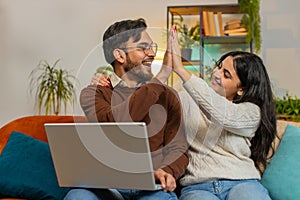 Cheerful young Indian family couple man woman using laptop and surprised with email winning lottery