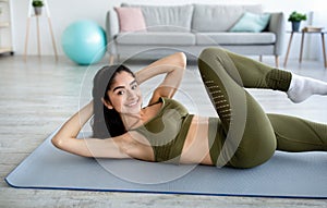 Cheerful young Indian woman exercising her core muscles on yoga mat at home